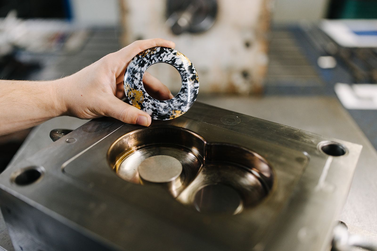 Hand hält rundes, marmoriertes Formteil über passender Metallform in einer Werkstatt